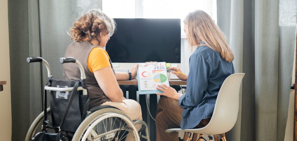 Two young contemporary female office workers discussing financial papers with charts and diagrams while one of them explaining data to colleague