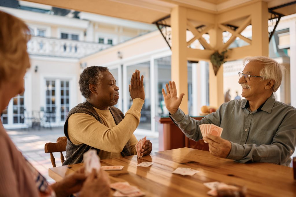 Two elderly adults playing cards and giving each other a high five